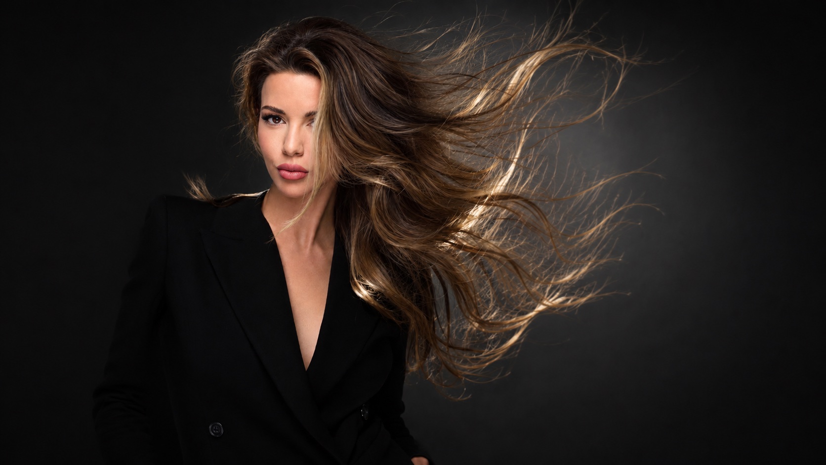 A woman in a black blazer with dark hair swept dramatically by wind, representing the House of Vue