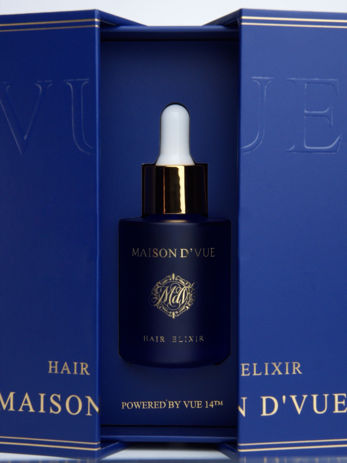 Close detail of the MAISON D'VUE Hair Elixir in its coffret, gold monogram and Powered by VUE 14 in relief