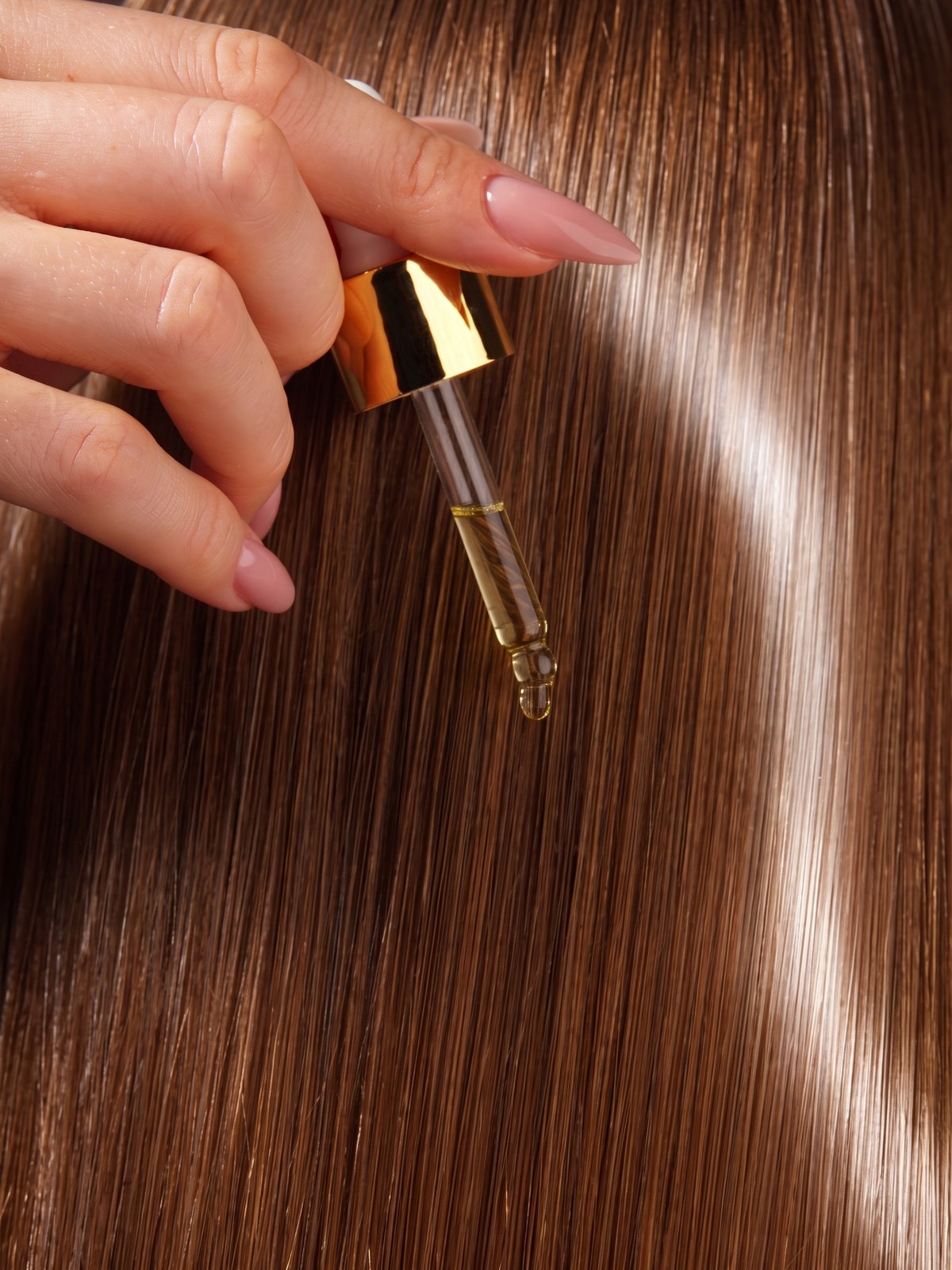 A golden drop of the elixir falling from the gold dropper onto glossy hair