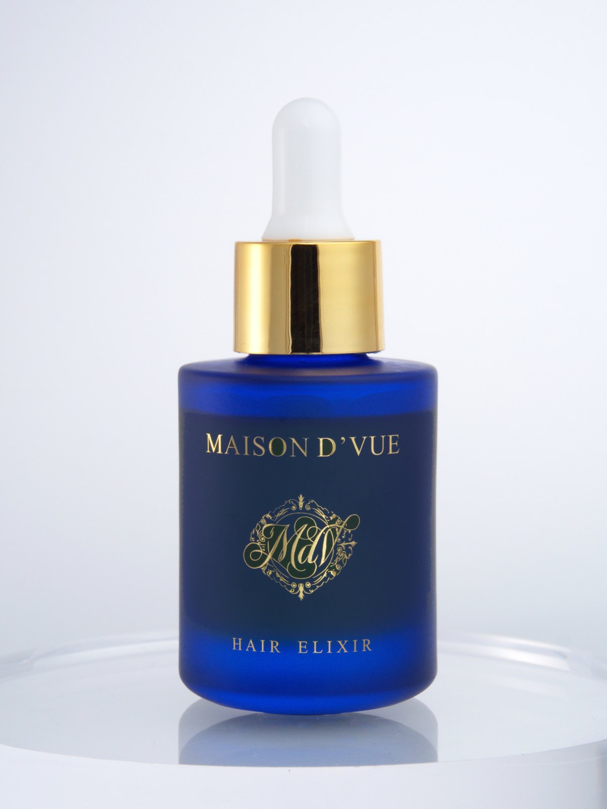 The MAISON D'VUE Hair Elixir, 30ml cobalt frosted glass with gold cap, lit against white