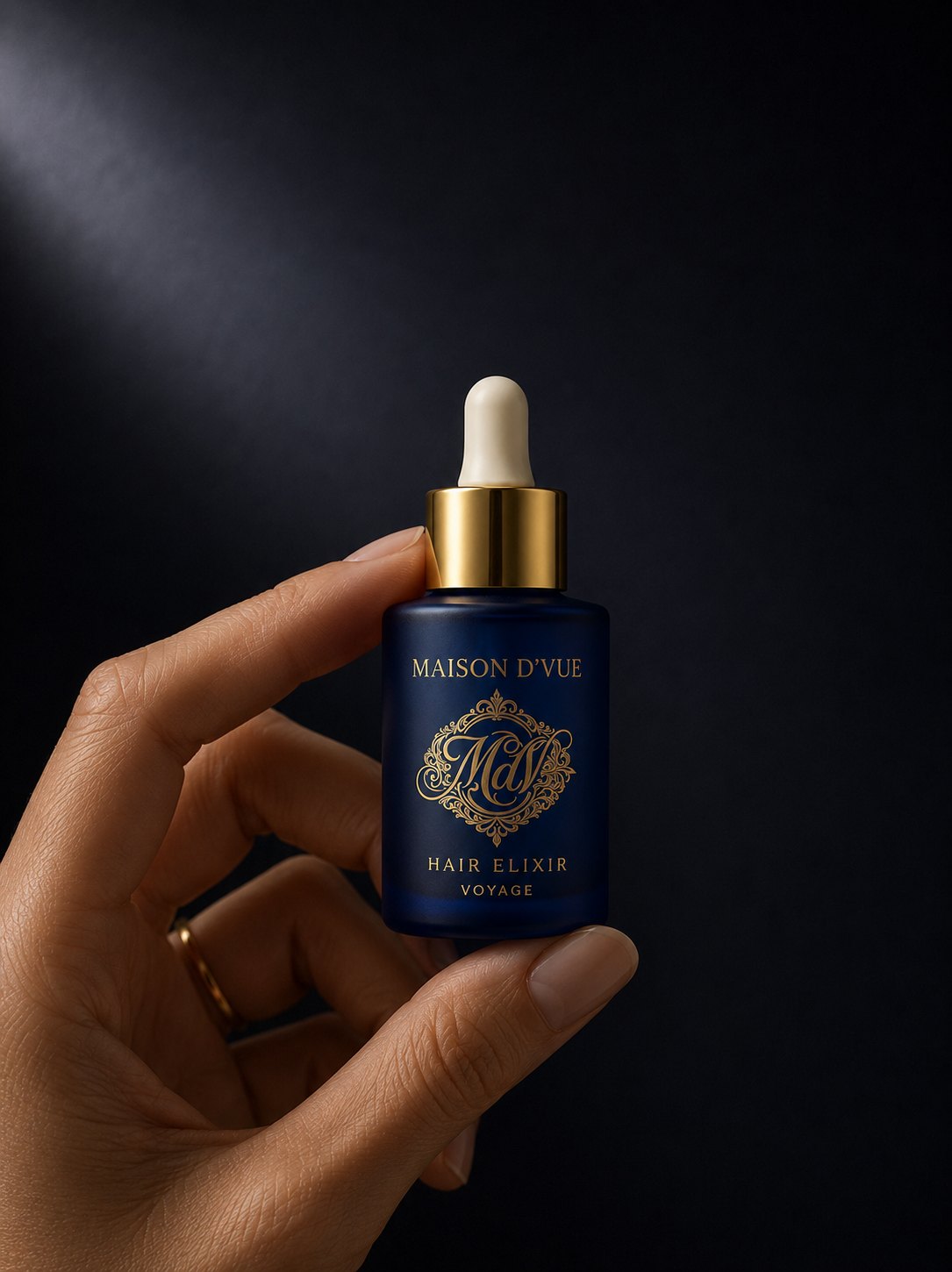 A hand holding the Voyage &mdash; 10ml MAISON D'VUE Hair Elixir travel size in cobalt frosted glass with matte gold cap, labeled Hair Elixir Voyage